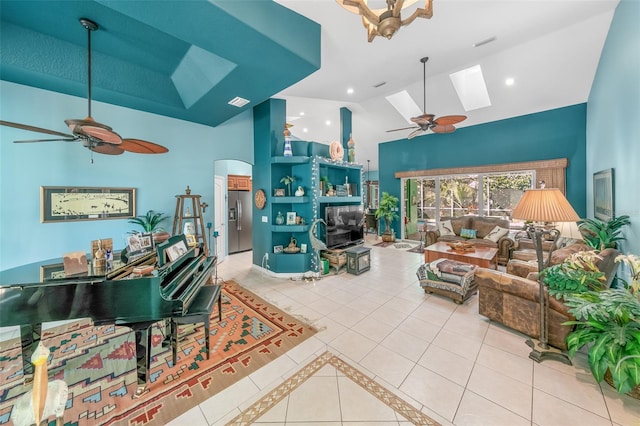 tiled living room featuring ceiling fan, a skylight, and high vaulted ceiling