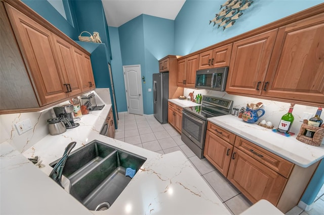 kitchen with appliances with stainless steel finishes, a towering ceiling, sink, decorative backsplash, and light tile patterned floors