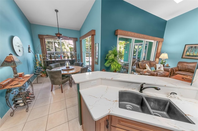 kitchen featuring pendant lighting, sink, light tile patterned floors, light stone counters, and vaulted ceiling