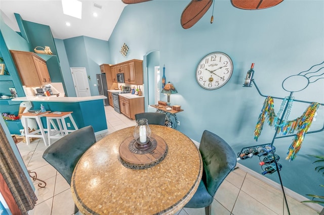 tiled dining room with high vaulted ceiling, ceiling fan, and a skylight