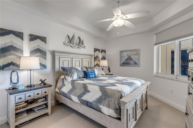 bedroom with ceiling fan, a tray ceiling, and light carpet