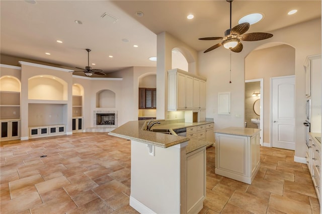 kitchen with a kitchen island, sink, a tiled fireplace, ceiling fan, and kitchen peninsula