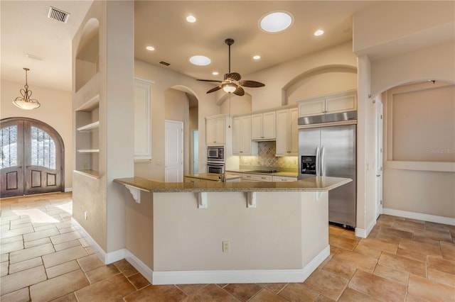 kitchen with light stone counters, built in appliances, a kitchen breakfast bar, kitchen peninsula, and backsplash