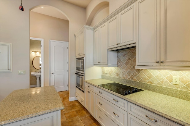 kitchen featuring backsplash, light stone countertops, sink, and black appliances