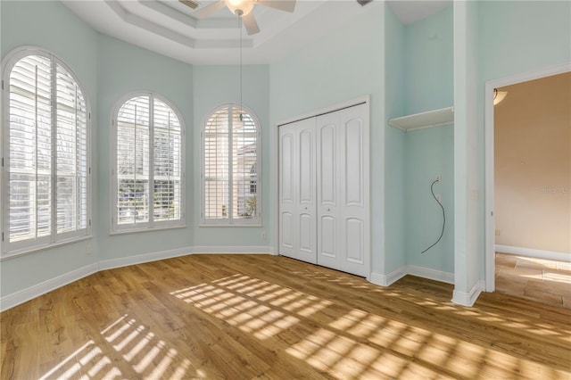 unfurnished bedroom with ceiling fan, a high ceiling, a tray ceiling, wood-type flooring, and a closet