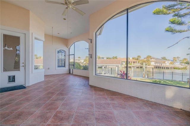 unfurnished sunroom with ceiling fan and a water view