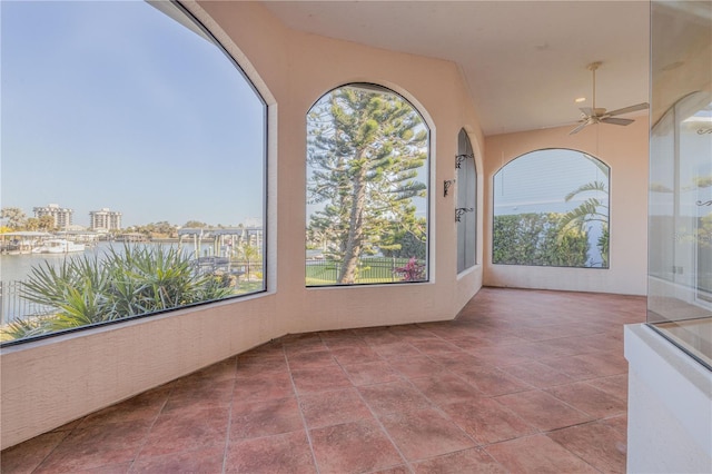 unfurnished sunroom featuring ceiling fan and a water view