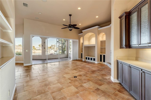 unfurnished living room featuring a wealth of natural light, built in features, and ceiling fan