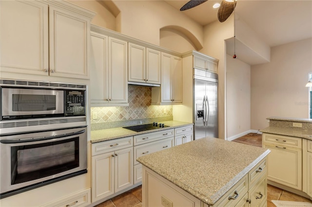 kitchen featuring backsplash, built in appliances, light stone countertops, a kitchen island, and cream cabinetry