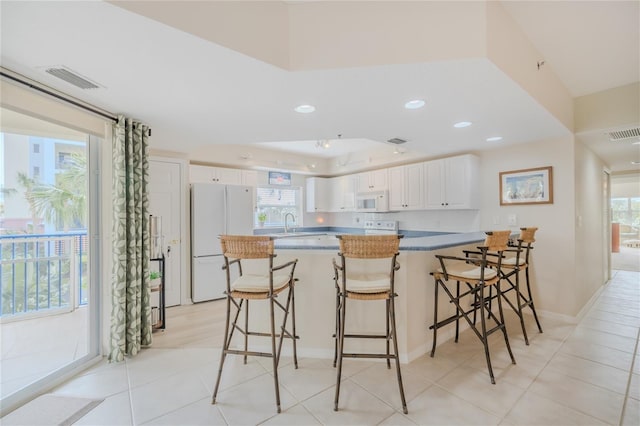 kitchen featuring white cabinetry, a kitchen bar, light tile patterned floors, kitchen peninsula, and white appliances