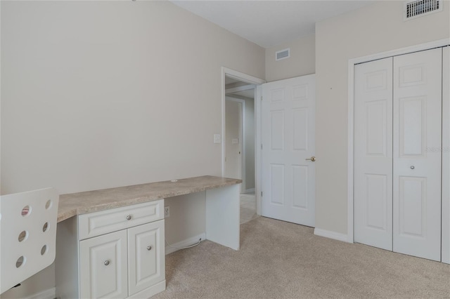 unfurnished office featuring built in desk and light colored carpet