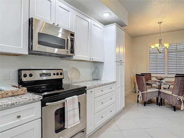 kitchen with appliances with stainless steel finishes, white cabinetry, light tile patterned flooring, light stone countertops, and a chandelier