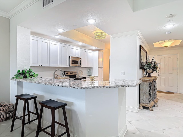 kitchen featuring ornamental molding, light stone counters, a peninsula, stainless steel appliances, and a kitchen bar