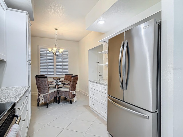 kitchen featuring freestanding refrigerator, white cabinetry, light stone countertops, a chandelier, and range with electric cooktop