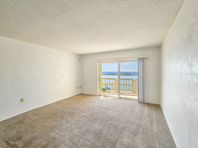 unfurnished room featuring carpet flooring, a textured ceiling, and a water view