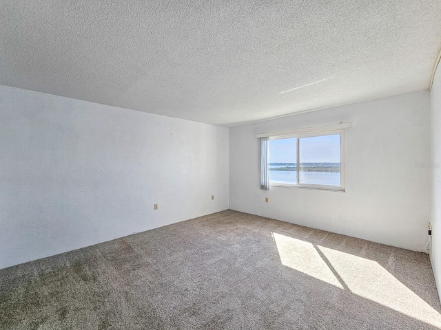 carpeted spare room featuring a water view and a textured ceiling