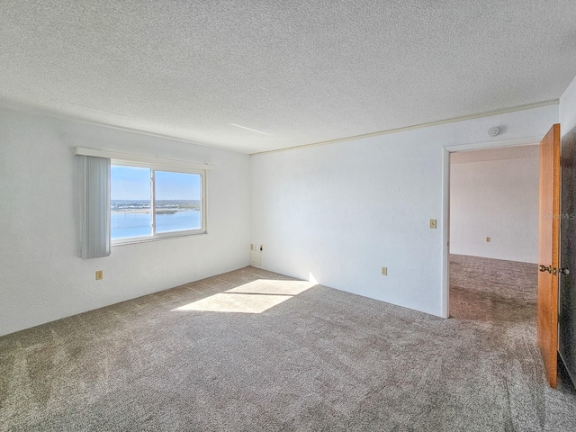 unfurnished room featuring a water view, carpet, and a textured ceiling