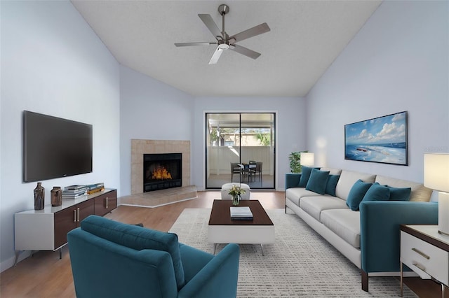 living room with ceiling fan, high vaulted ceiling, a fireplace, light hardwood / wood-style floors, and a textured ceiling