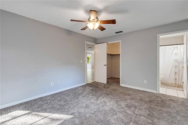 unfurnished bedroom with connected bathroom, a spacious closet, a textured ceiling, a closet, and light colored carpet