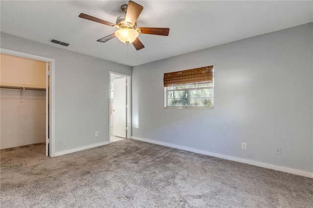 unfurnished bedroom featuring carpet floors, a walk in closet, ceiling fan, a textured ceiling, and a closet