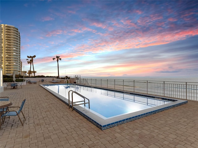 pool at dusk featuring a water view and a patio area