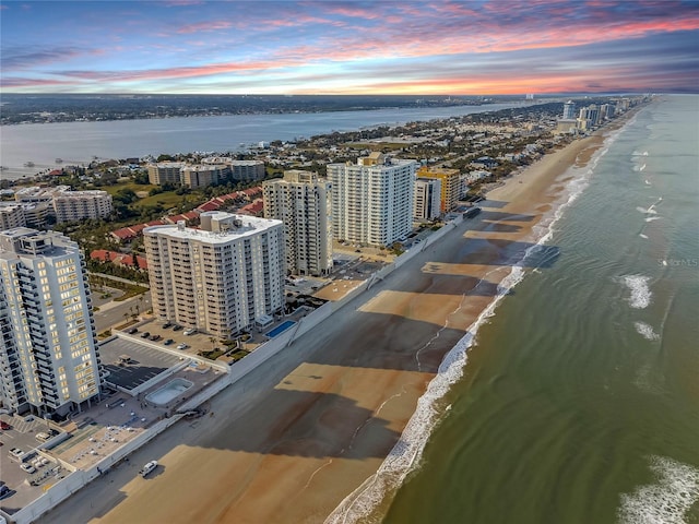 aerial view at dusk featuring a view of the beach and a water view