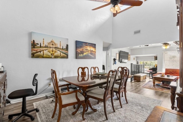 dining space with a towering ceiling, ceiling fan, and light wood-type flooring