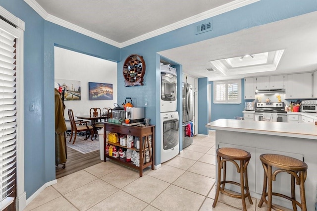 kitchen featuring stainless steel appliances, stacked washing maching and dryer, ornamental molding, and light tile patterned floors