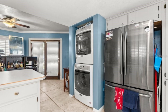 clothes washing area with stacked washer and dryer, a textured ceiling, light tile patterned floors, ornamental molding, and ceiling fan