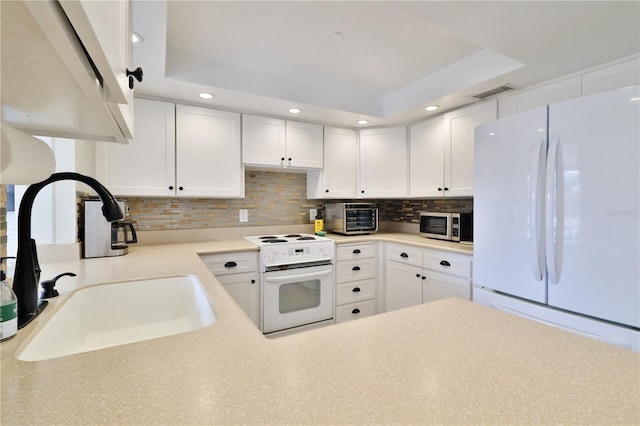 kitchen with a raised ceiling, white cabinetry, sink, and white appliances