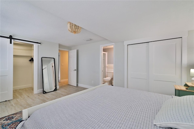 bedroom featuring connected bathroom, a barn door, a closet, and light wood-type flooring