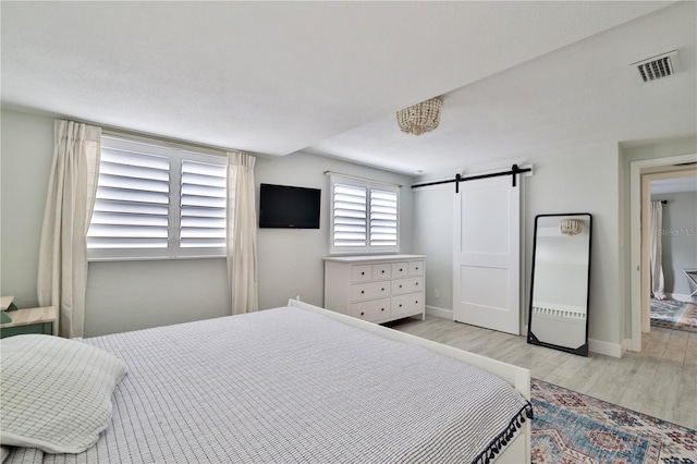 bedroom with a barn door and light wood-type flooring