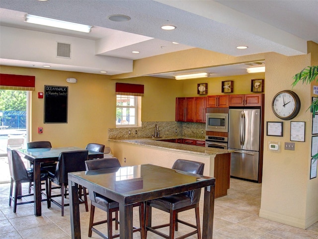 kitchen featuring sink, backsplash, stainless steel appliances, light tile patterned flooring, and kitchen peninsula