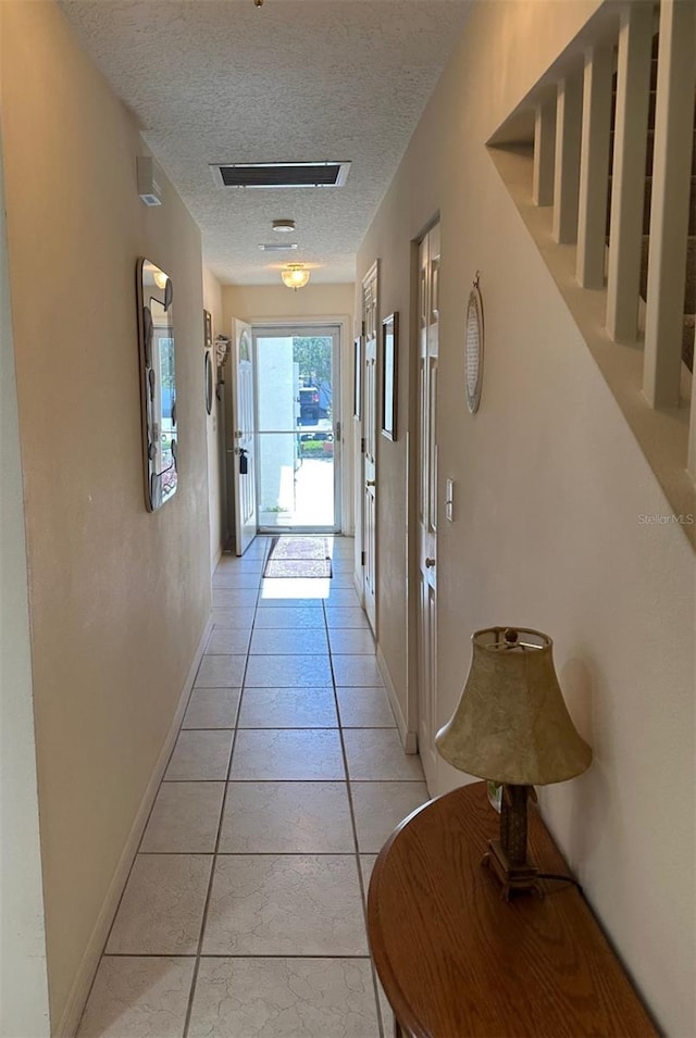 hall with visible vents, a textured ceiling, and baseboards