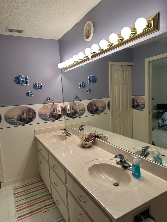 ensuite bathroom with a textured ceiling, visible vents, and a sink