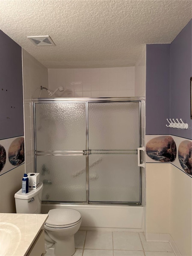 full bathroom featuring toilet, a textured ceiling, shower / bath combination with glass door, tile patterned flooring, and vanity