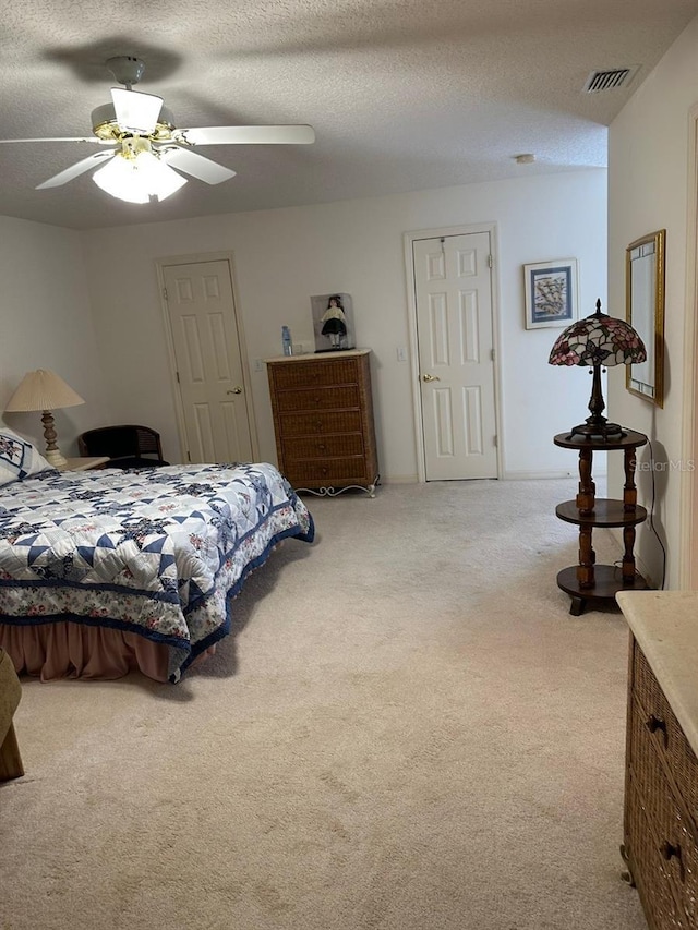 carpeted bedroom with visible vents, a textured ceiling, and ceiling fan