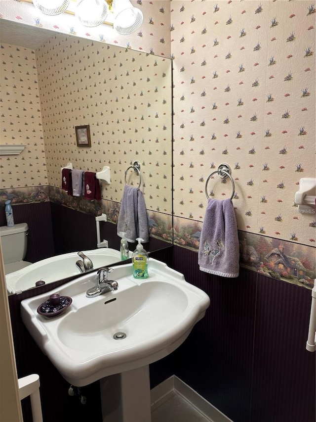 half bath featuring a sink, toilet, and wallpapered walls