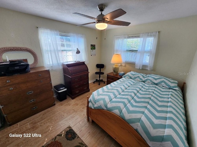 bedroom with multiple windows, ceiling fan, a textured ceiling, and light hardwood / wood-style flooring