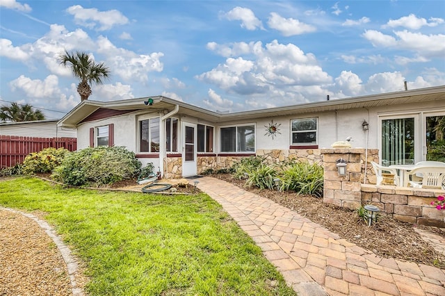 view of front of property featuring stone siding, fence, a front lawn, and stucco siding