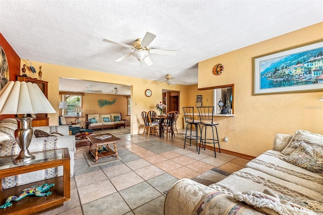 living room with light tile patterned floors, a textured wall, a textured ceiling, and ceiling fan