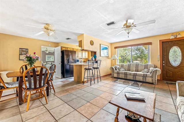 living area featuring light tile patterned floors, a textured ceiling, visible vents, and a ceiling fan