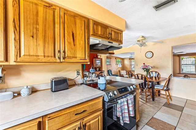 kitchen with brown cabinetry, a ceiling fan, light countertops, stainless steel range with electric cooktop, and under cabinet range hood