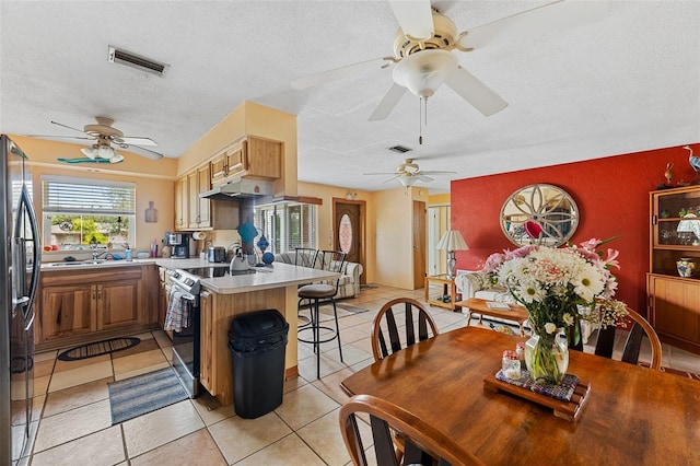 kitchen with a breakfast bar area, a peninsula, visible vents, freestanding refrigerator, and stainless steel electric range oven