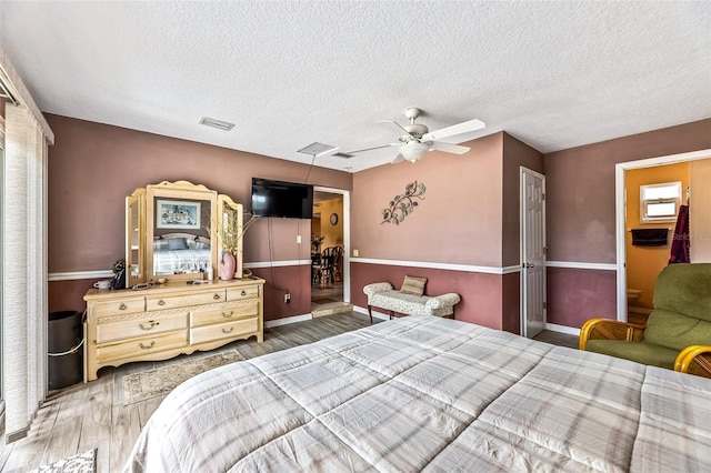 bedroom with a textured ceiling, ceiling fan, wood finished floors, and visible vents