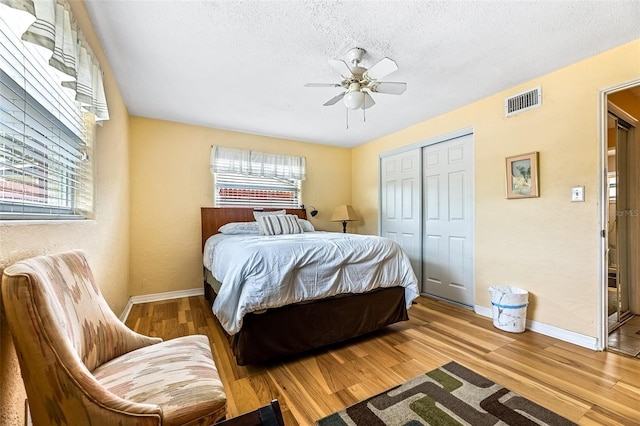 bedroom featuring a textured ceiling, wood finished floors, visible vents, baseboards, and a closet