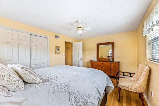 bedroom with baseboards, visible vents, a ceiling fan, wood finished floors, and a closet