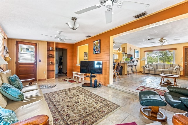 living room featuring a textured ceiling, wood walls, visible vents, and a ceiling fan