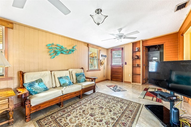 living area with a textured ceiling, light tile patterned flooring, visible vents, and a ceiling fan