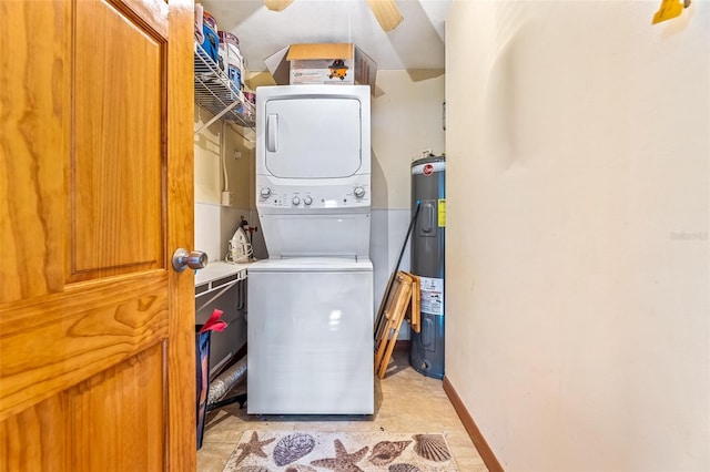 laundry area featuring laundry area, baseboards, electric water heater, and stacked washer and clothes dryer